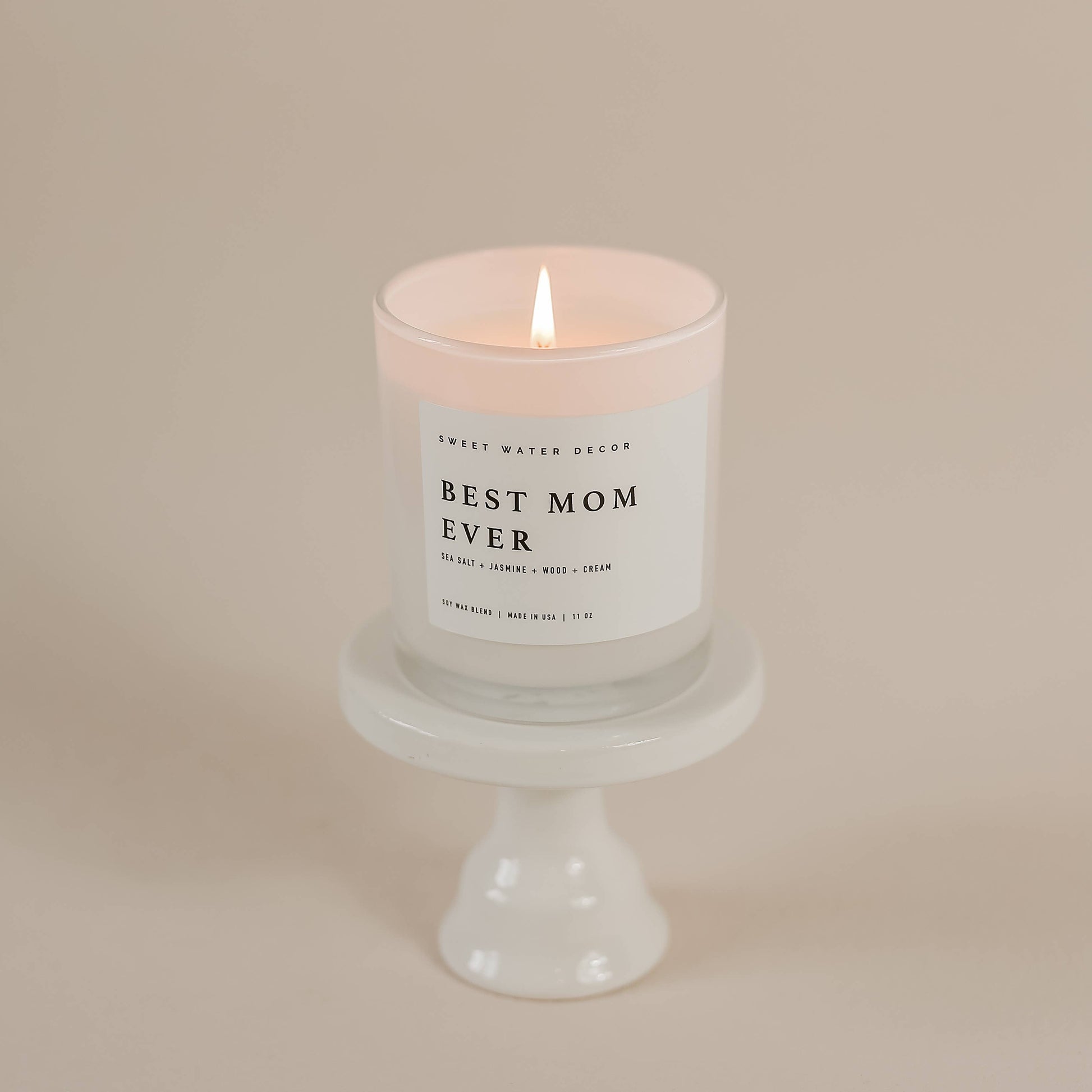 Candle with 'Best Mom Ever' label on a white pedestal against a beige background