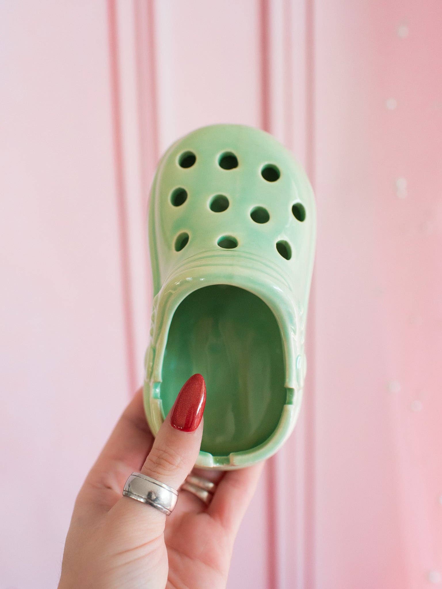 Green clog shaped tray held by a hand with red nail polish against a pink background