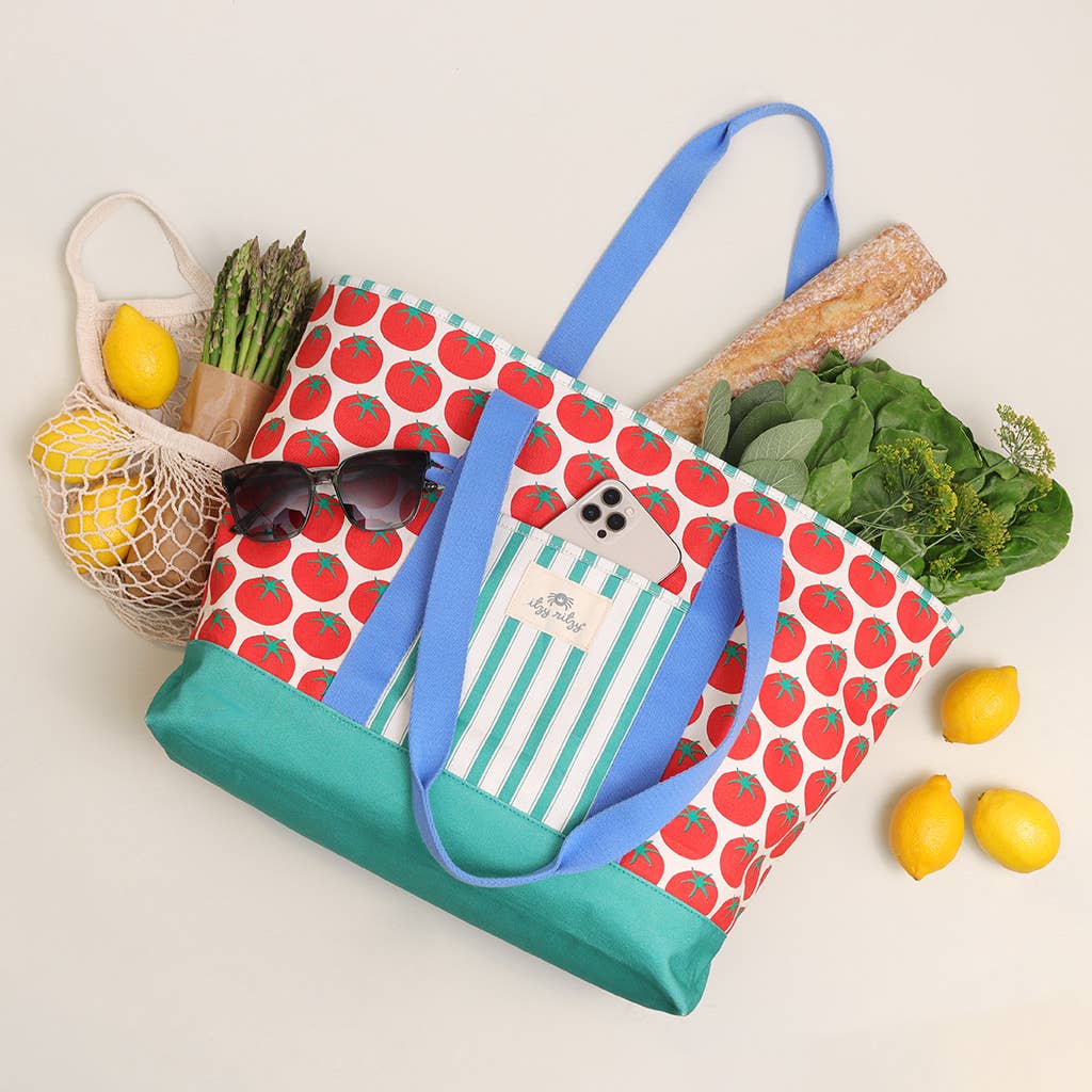 Tote bag with tomato pattern, green base and blue handles with tomato pattern filled with groceries on a light background