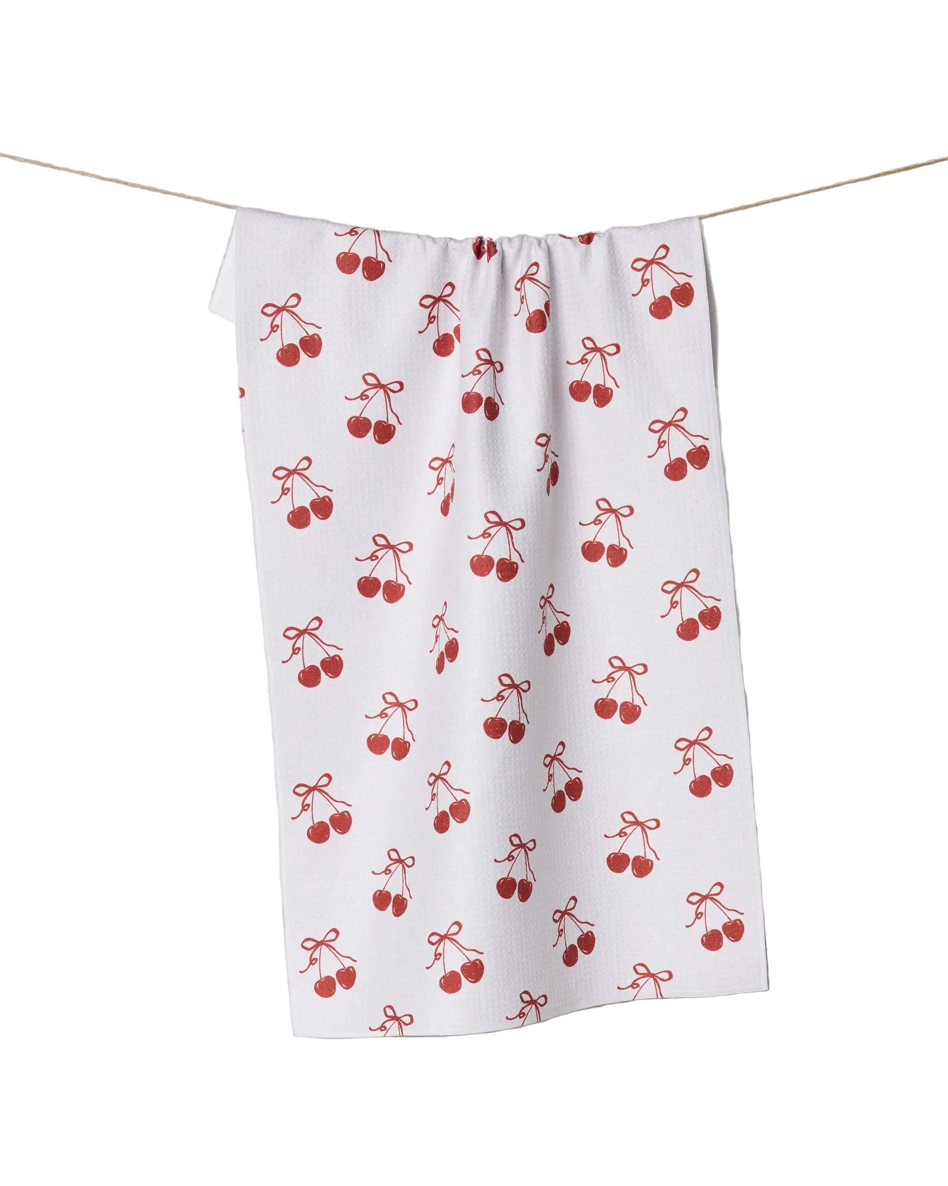 White tea towel with red cherry pattern hanging on a line against a white background