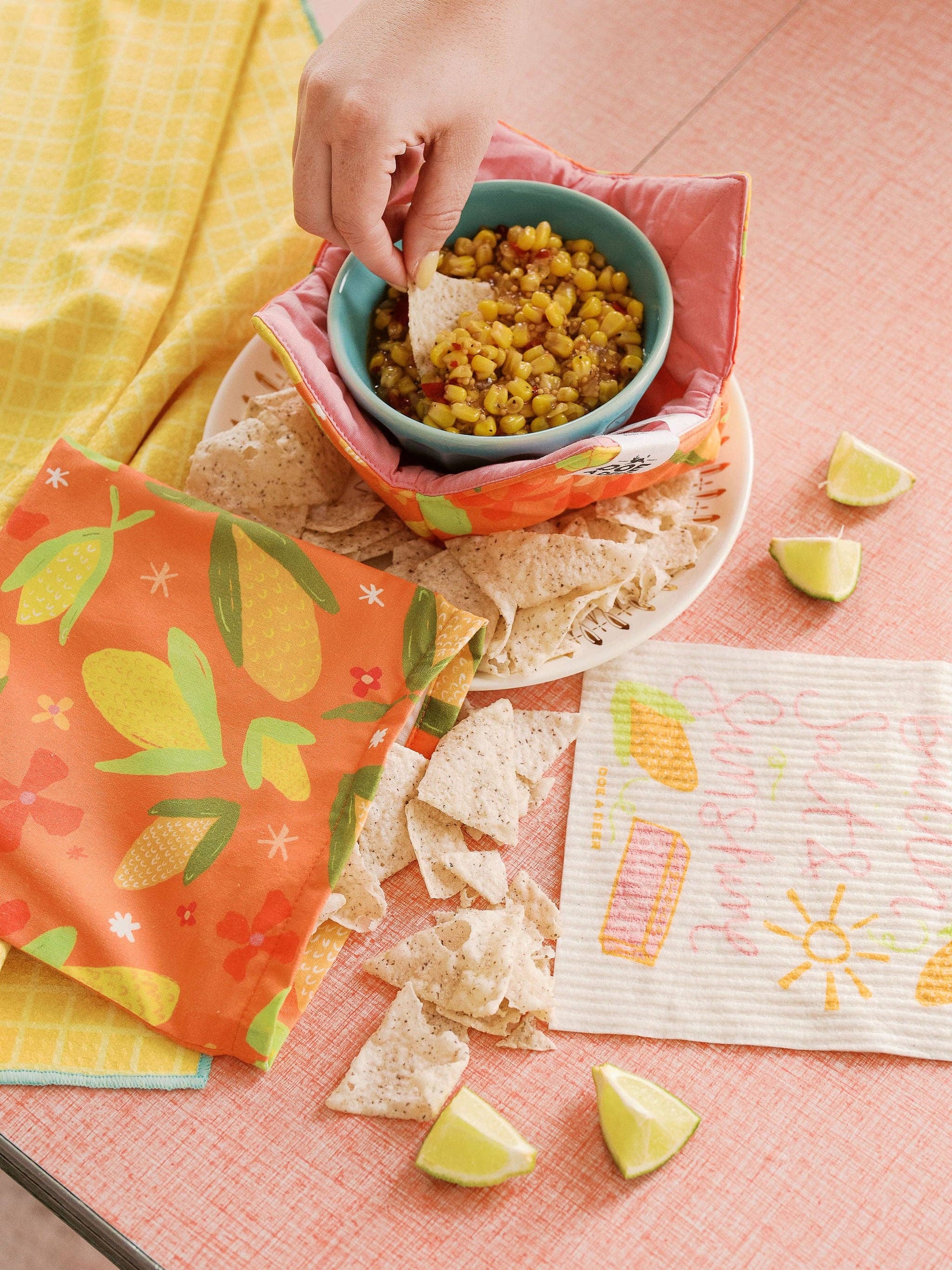 Person dipping tortilla chip into a bowl of salsa on a colorful tablecloth.
