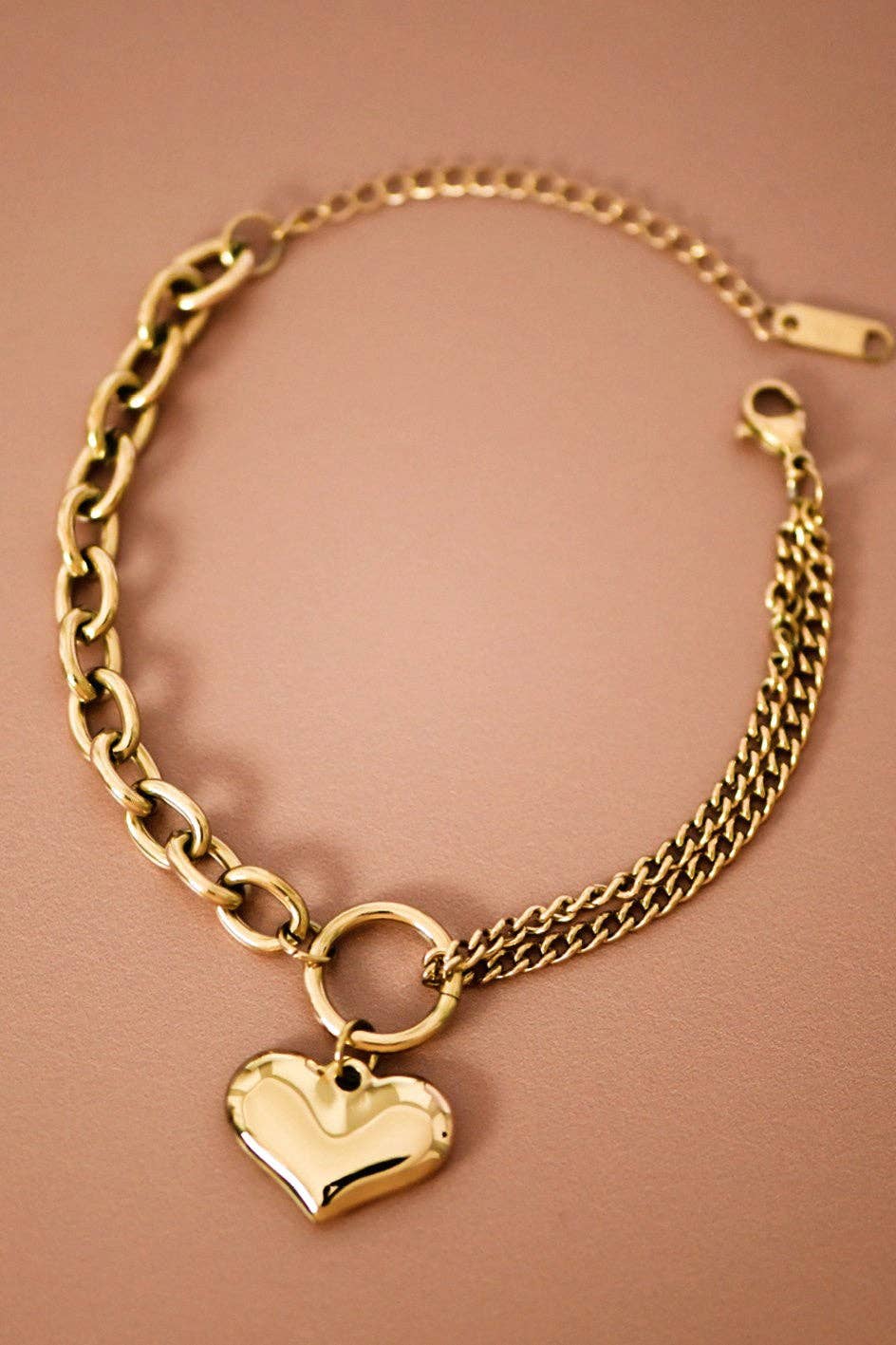 Gold chain bracelet with a heart-shaped charm on a brown background
