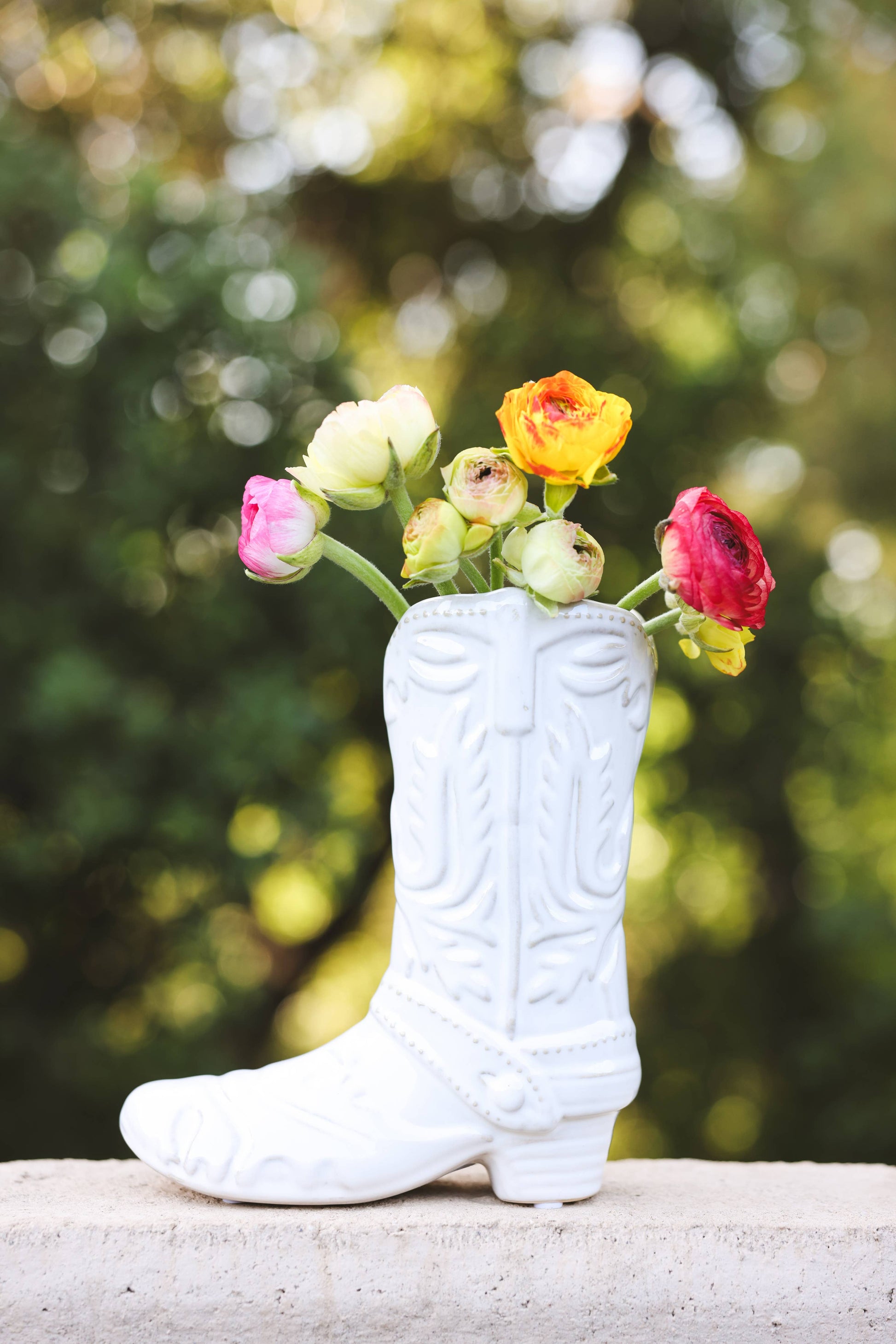 White cowboy boot vase with colorful flowers inside against a blurred green background