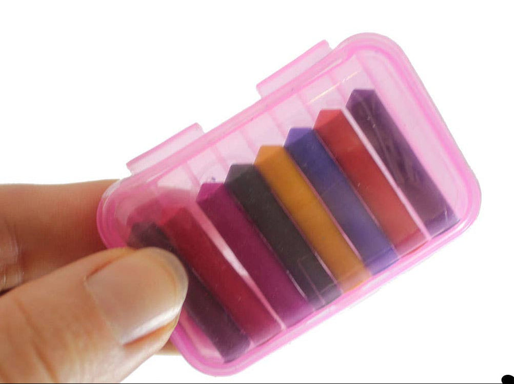 Hand holding a pink container with colorful crayons on a white background