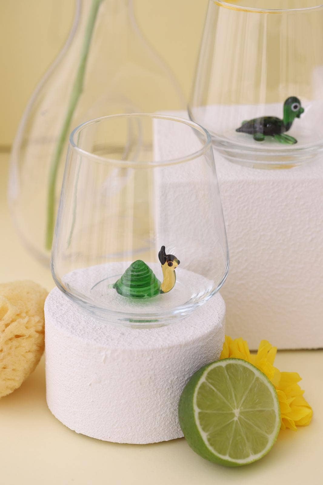 Decorative glass with turtle figurine on a white base, surrounded by lime and flowers.