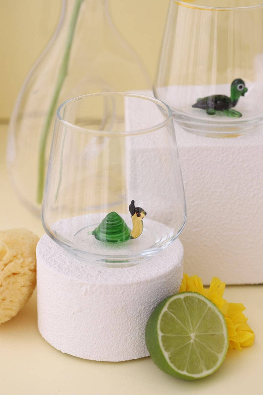 Decorative glass with turtle figurine on a white base, surrounded by lime and flowers.