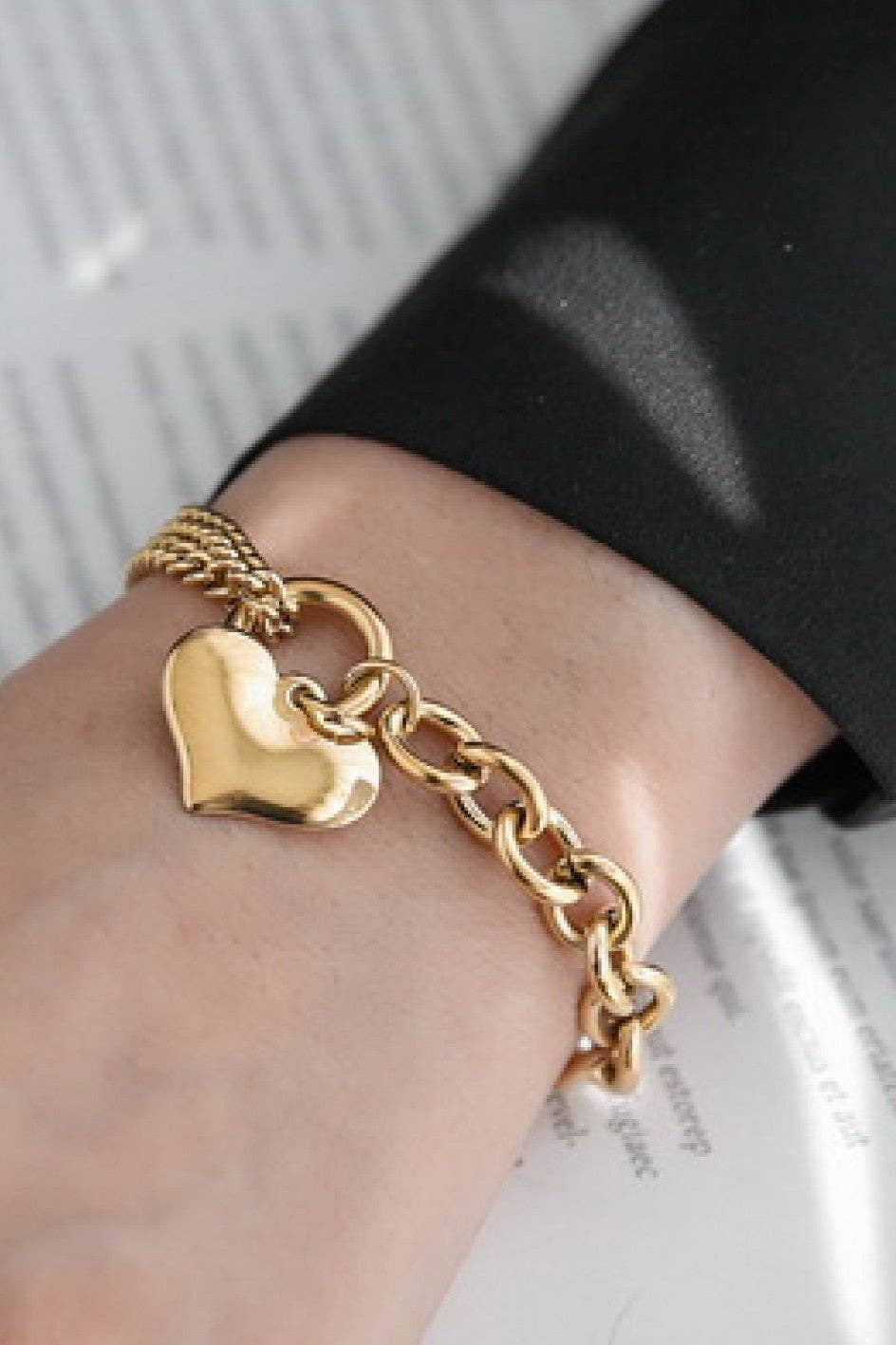 Gold chain bracelet with a heart-shaped charm on a wrist.