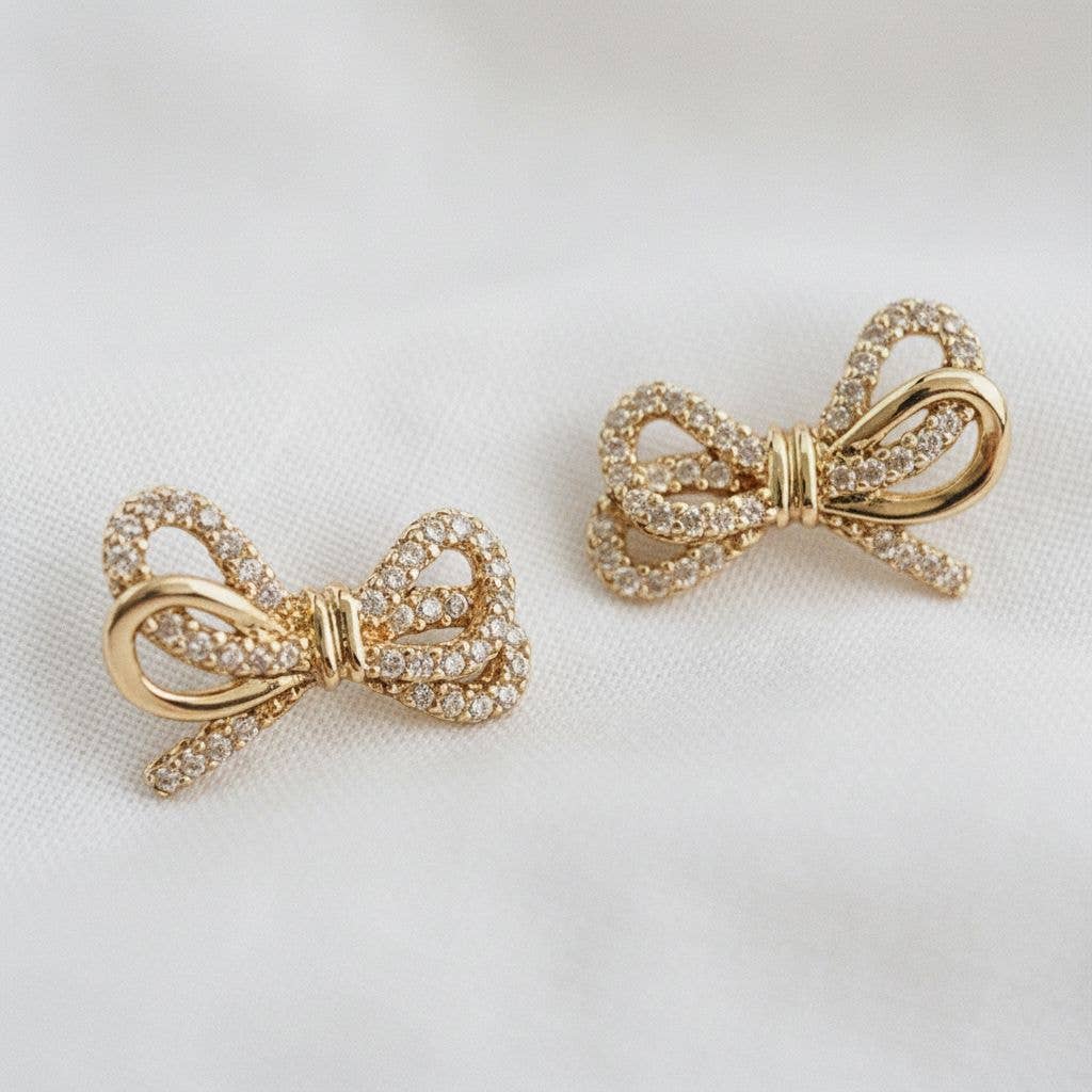 Gold bow-shaped earrings with gemstones on a light background