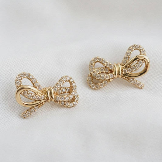 Gold bow-shaped earrings with gemstones on a light background