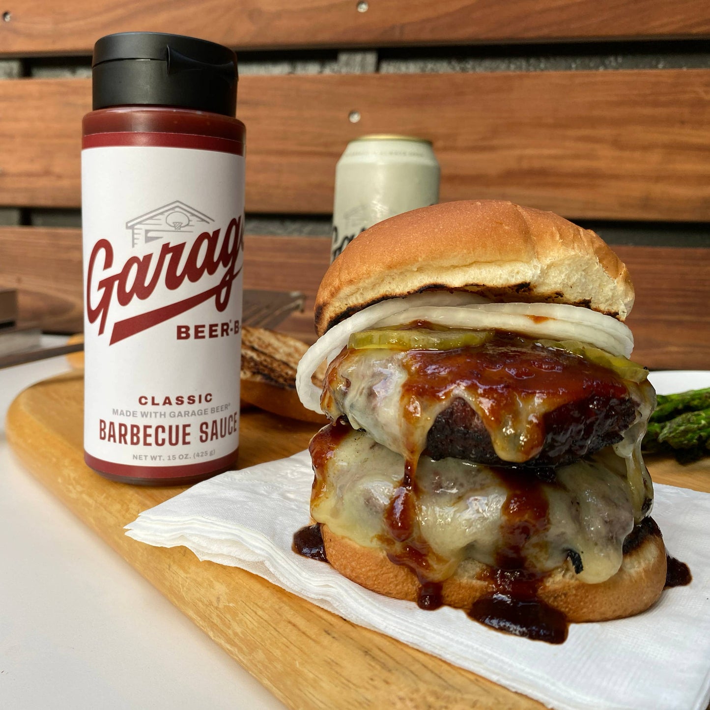 Burger with barbecue sauce and a bottle of Garage Beer Classic Barbecue Sauce on a wooden surface.