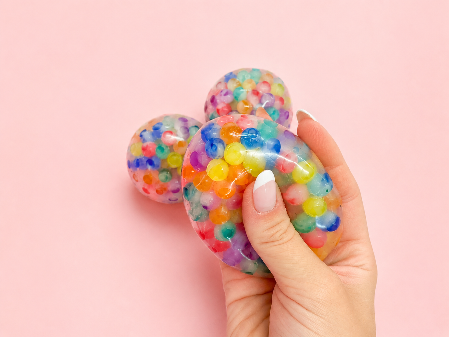 Colorful stress ball held by a hand on a pink background