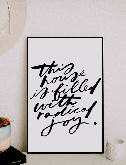 Framed print with 'This house is filled with radical joy' text on a white wall.