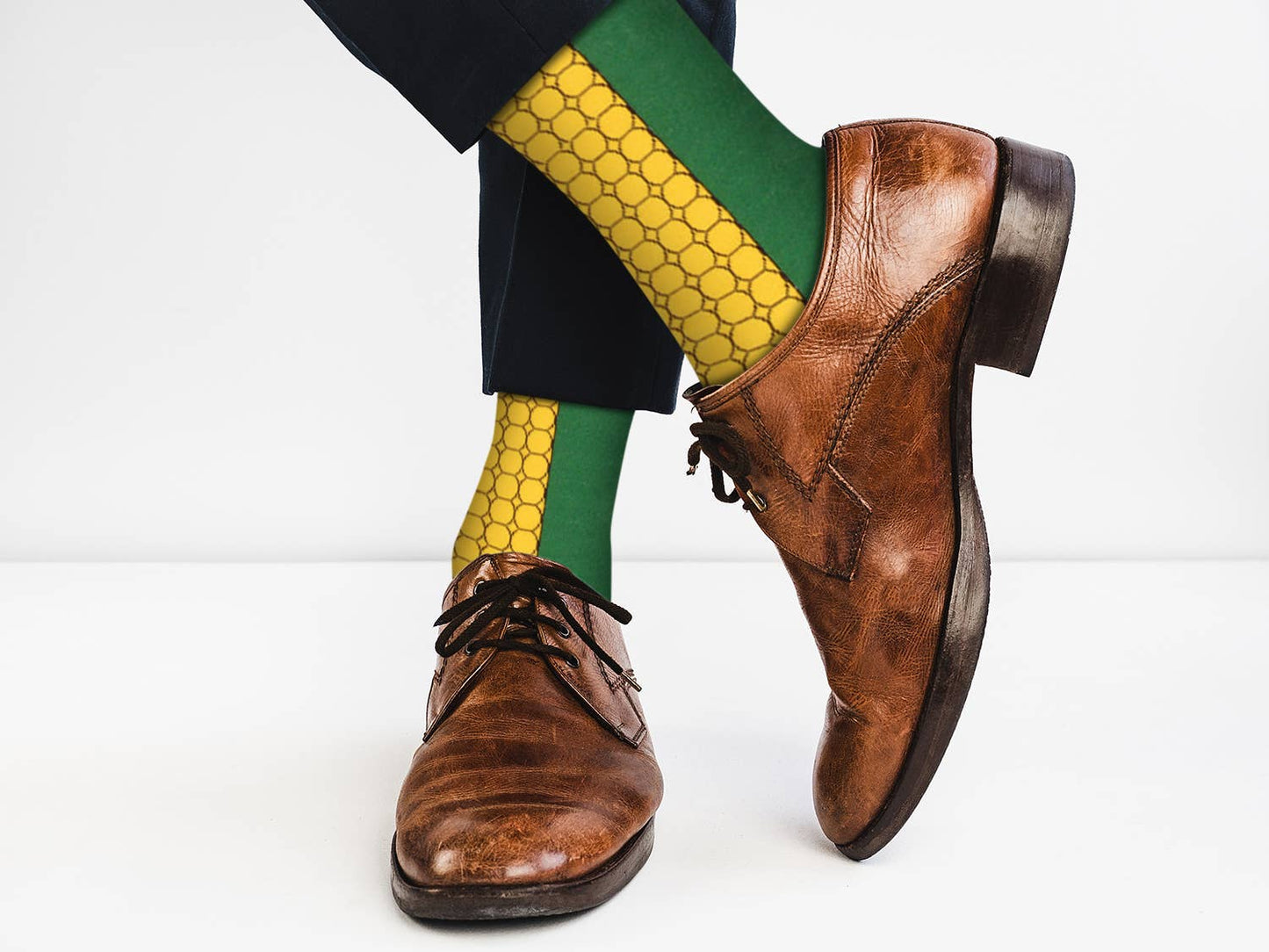 Brown dress shoes with green and yellow patterned socks on a white background