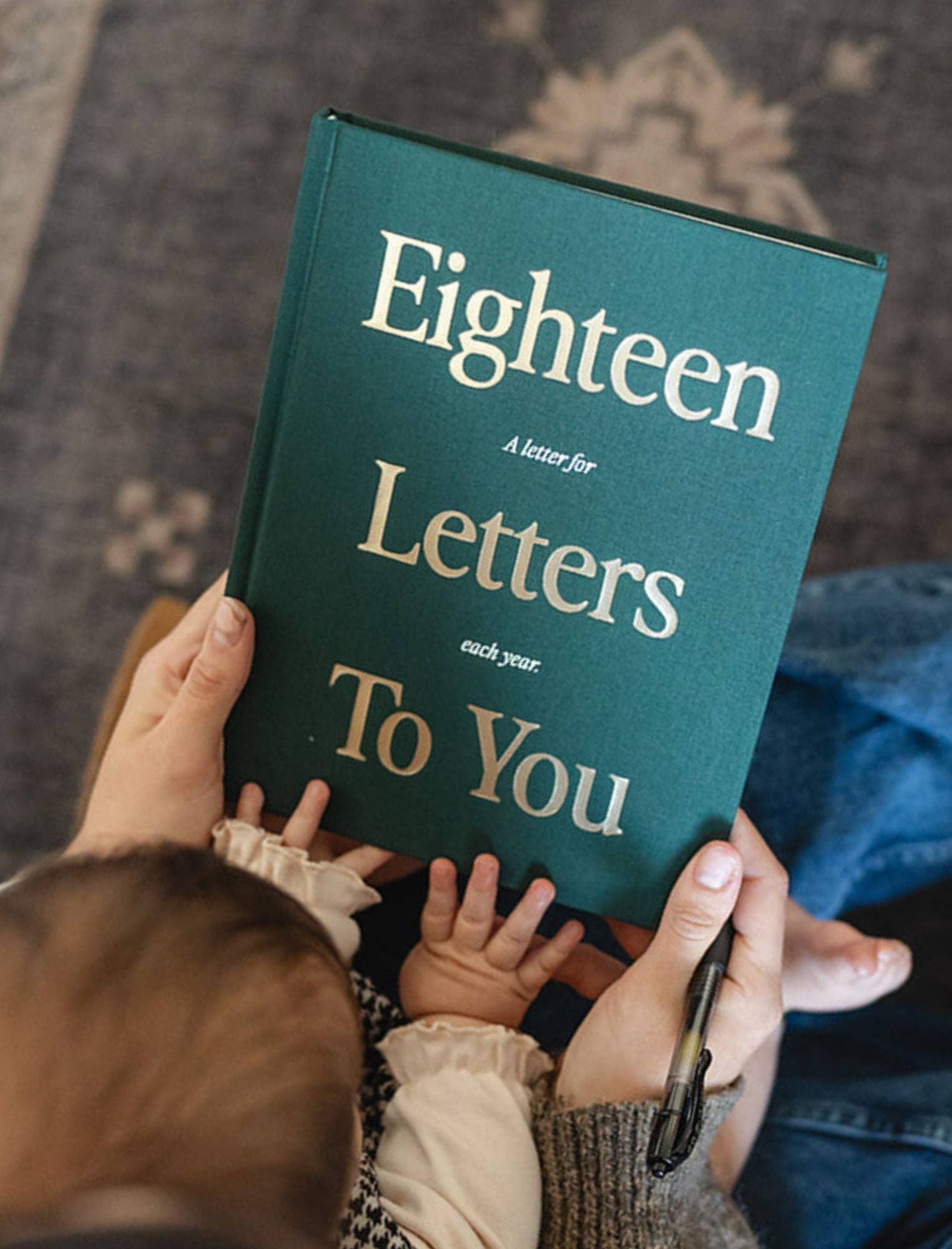 Person holding a book titled 'Eighteen Letters to You' with a child's hand on the cover.