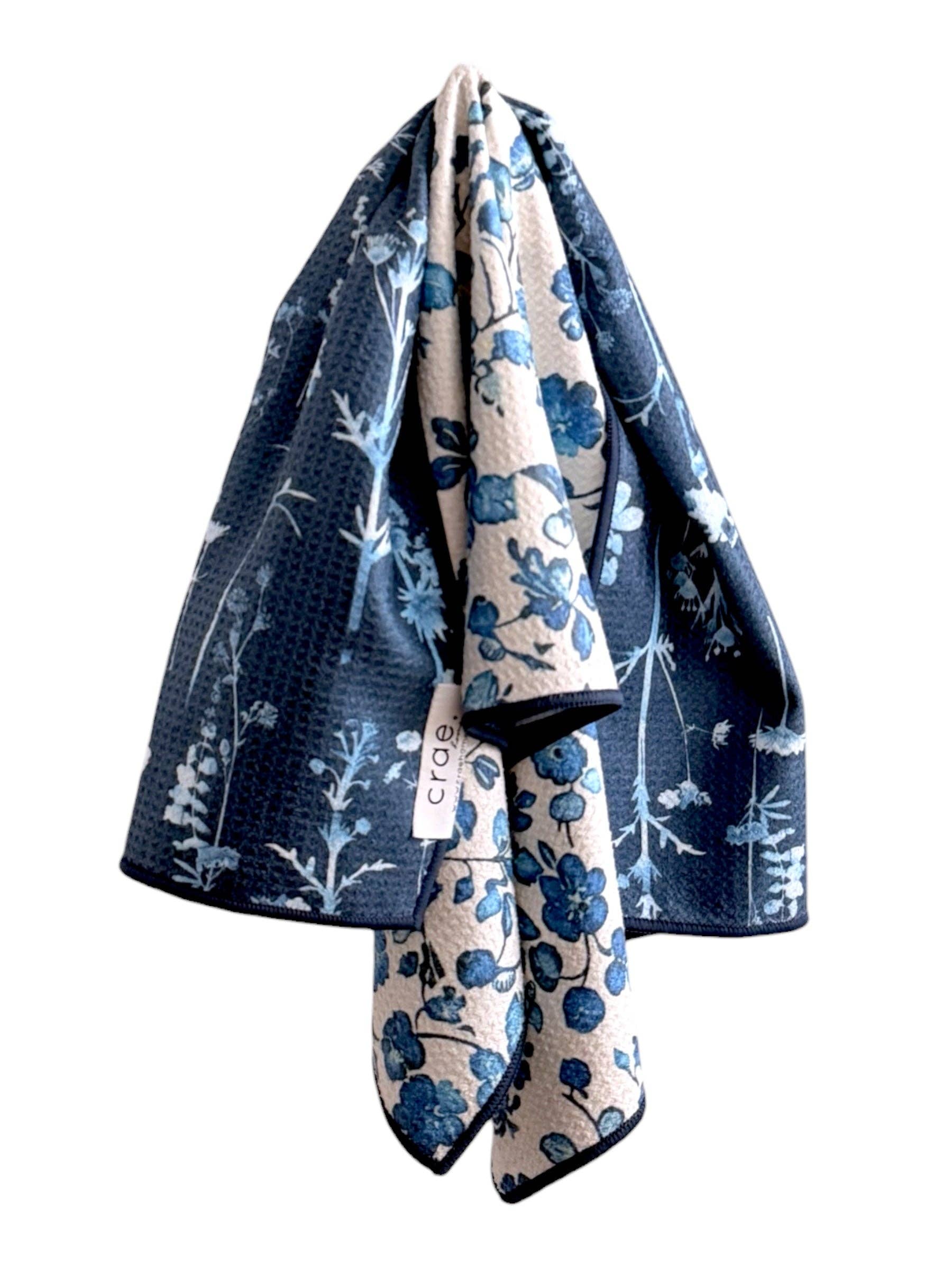 Two floral-patterned towels, one blue and one beige with white patterns, draped over each other on a white background.