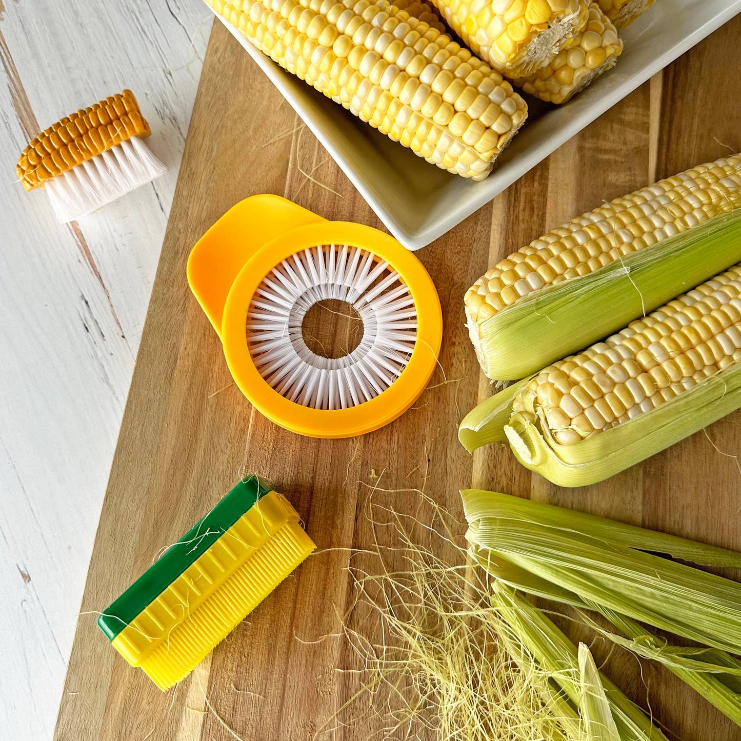 Corn husking tool on a wooden surface with corn ears and husks.