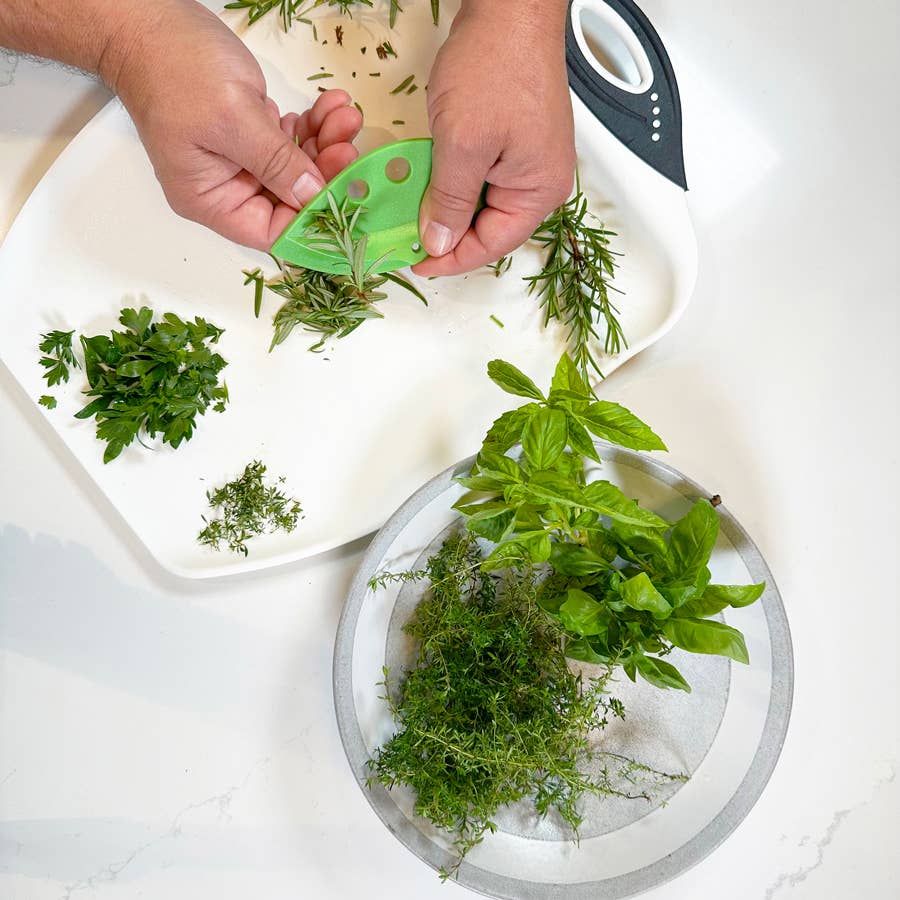 Hands using a green herb stripper to pluck fresh herbs from a white plate.