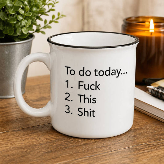 White mug with humorous text on a wooden surface with a plant and candle in the background