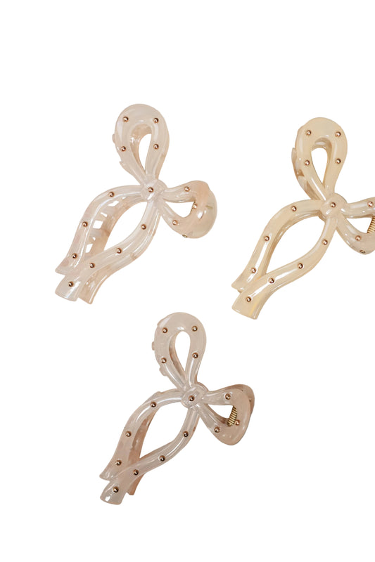 Three bow-shaped earrings on a textured gray surface
