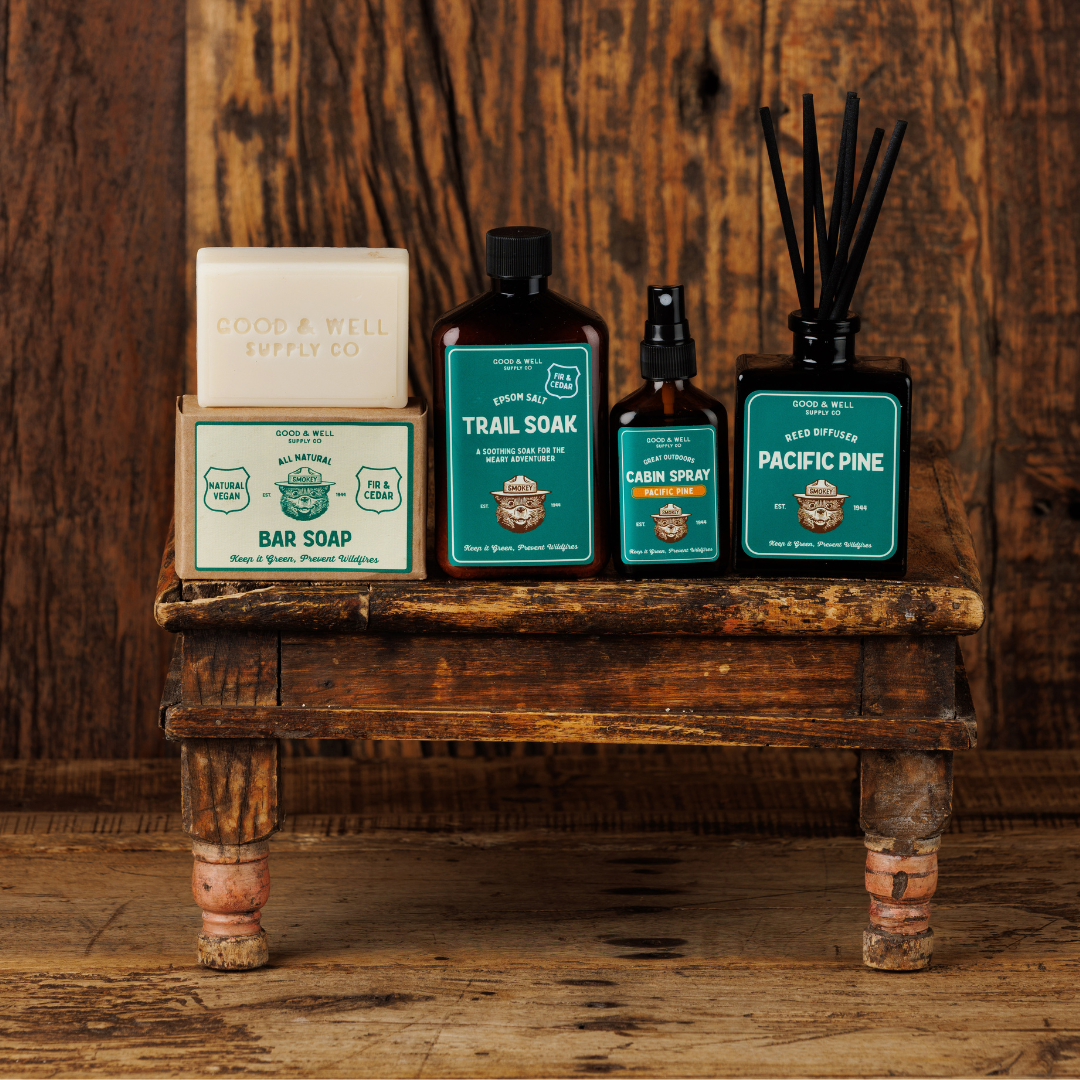 Collection of natural products including a bar soap, trail soap, and diffuser on a wooden shelf against a rustic wooden wall.