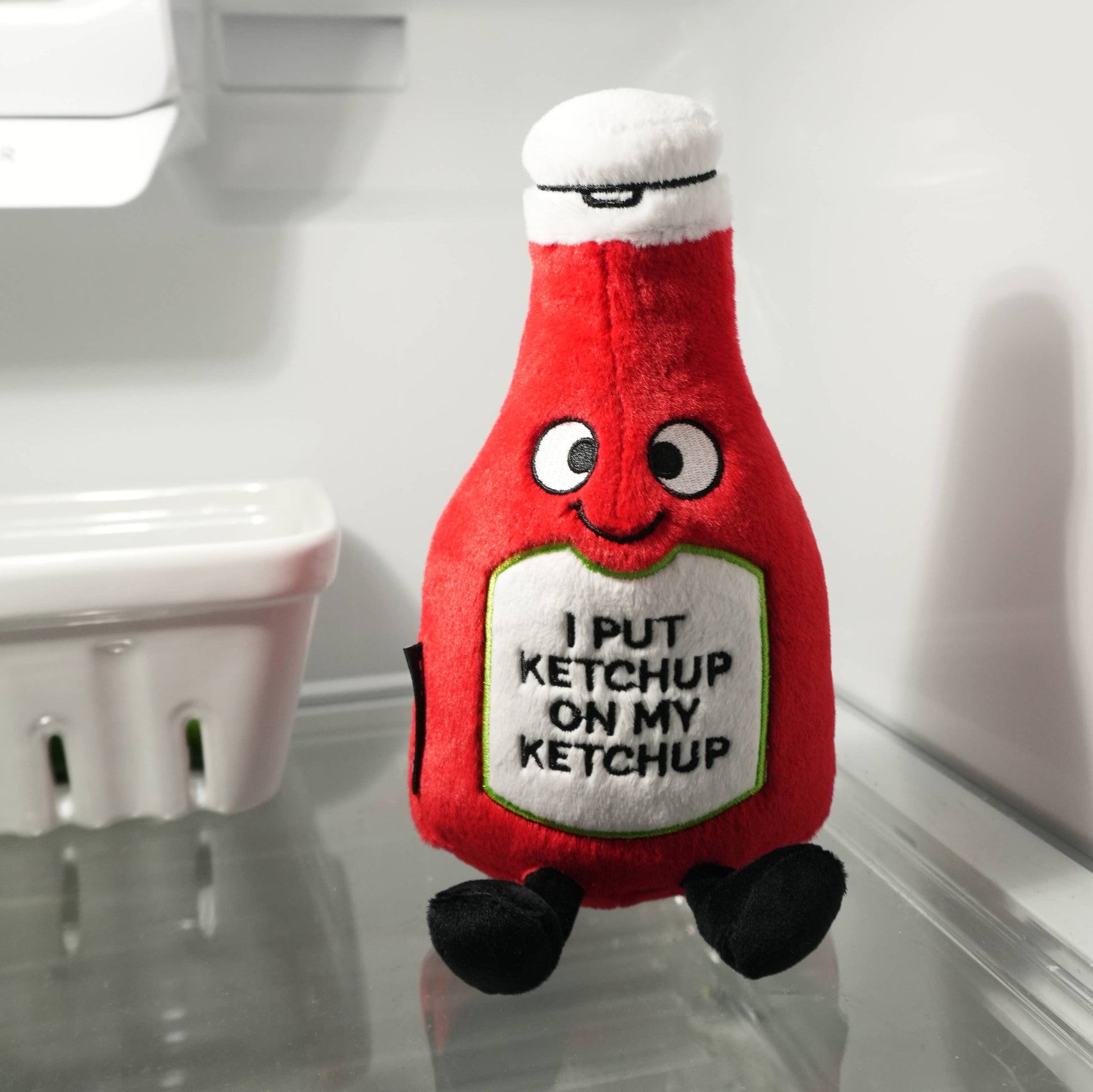 Plush toy resembling a ketchup bottle with text on a reflective surface.