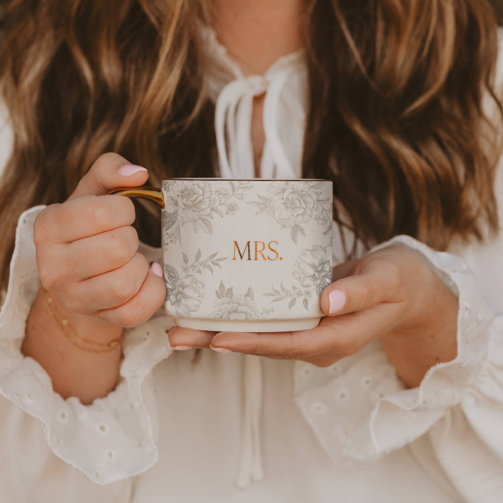 Person holding a mug with 'MRS' on it, wearing a white blouse.