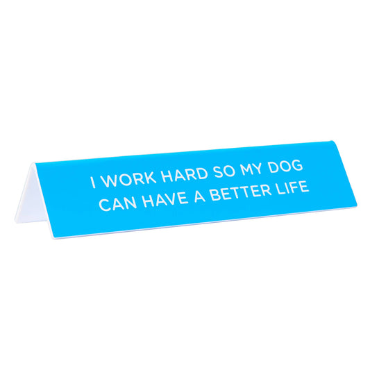 blue desk sign with the text "i work had so my dog can have a better life" sitting on a white background