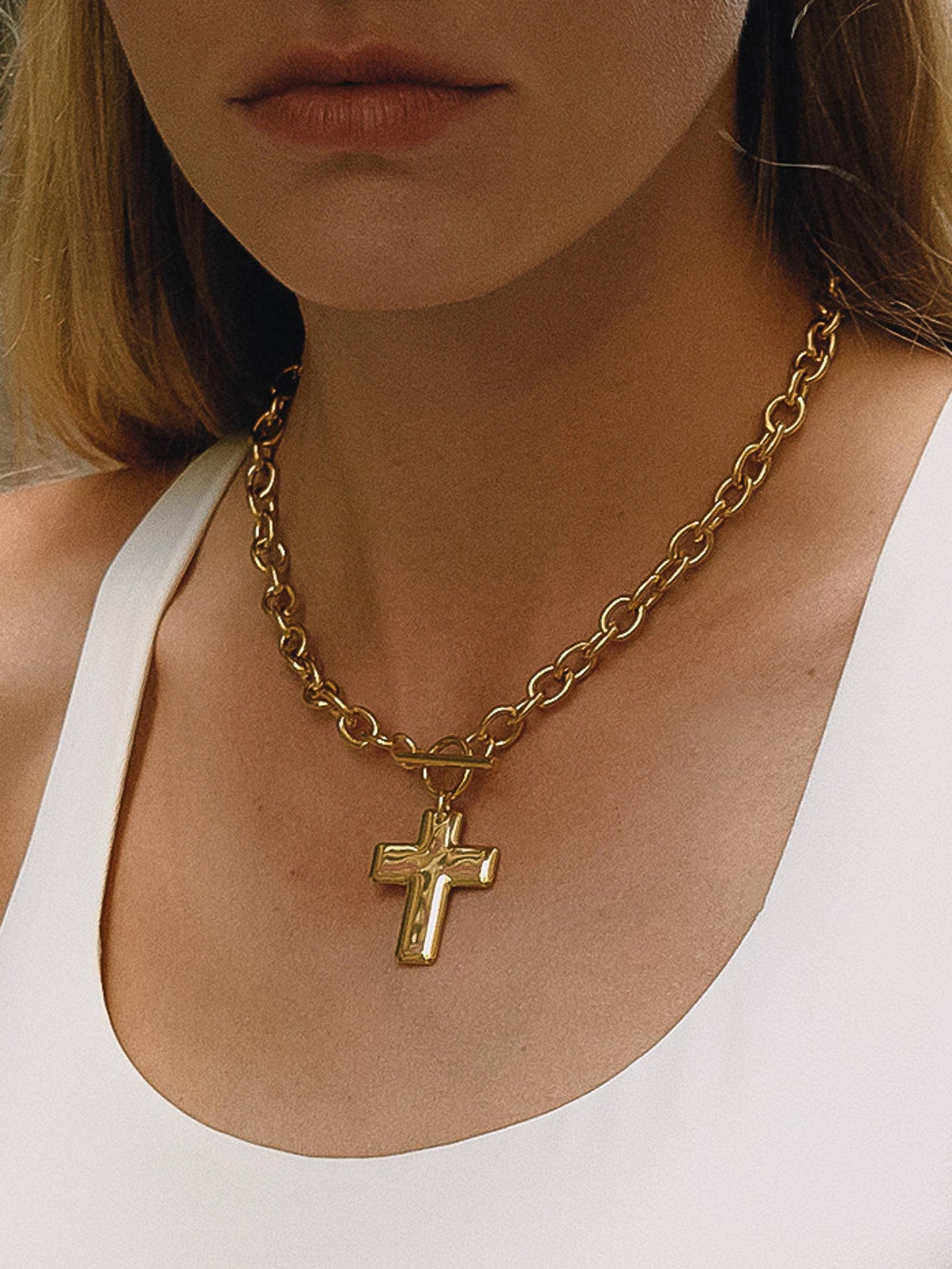 Gold chain necklace with a cross pendant worn by a person in a white top.