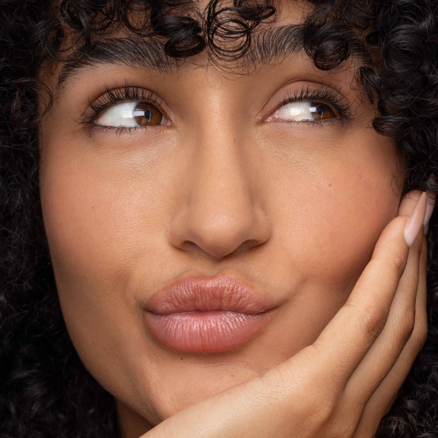 Close-up of a woman with curly hair and hand on face