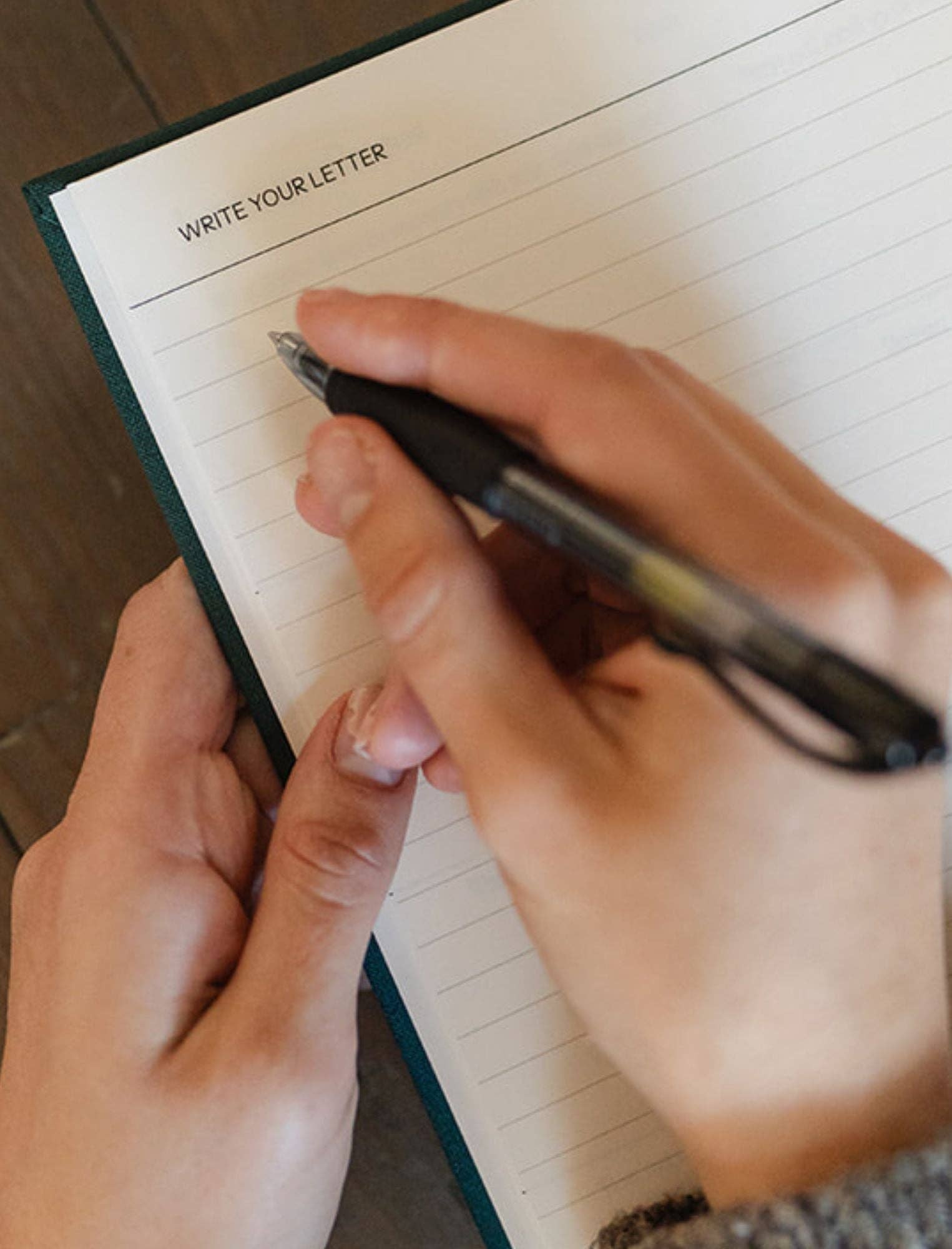 Person writing in a notebook with lined paper and text 'Write Your Letter'.