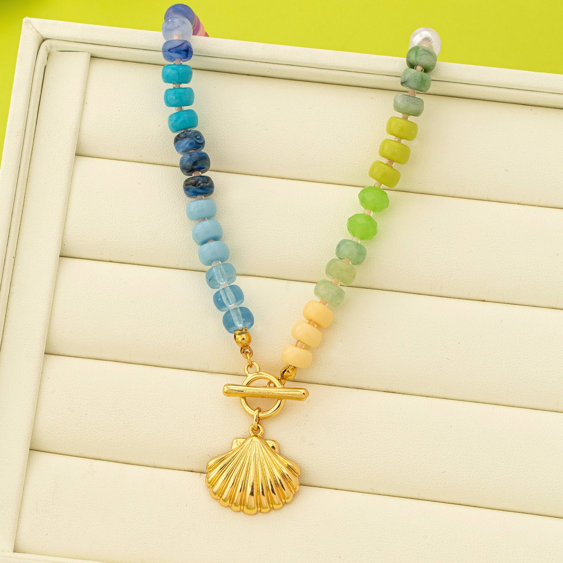 Necklace with colorful beads and a gold shell pendant on a wooden surface