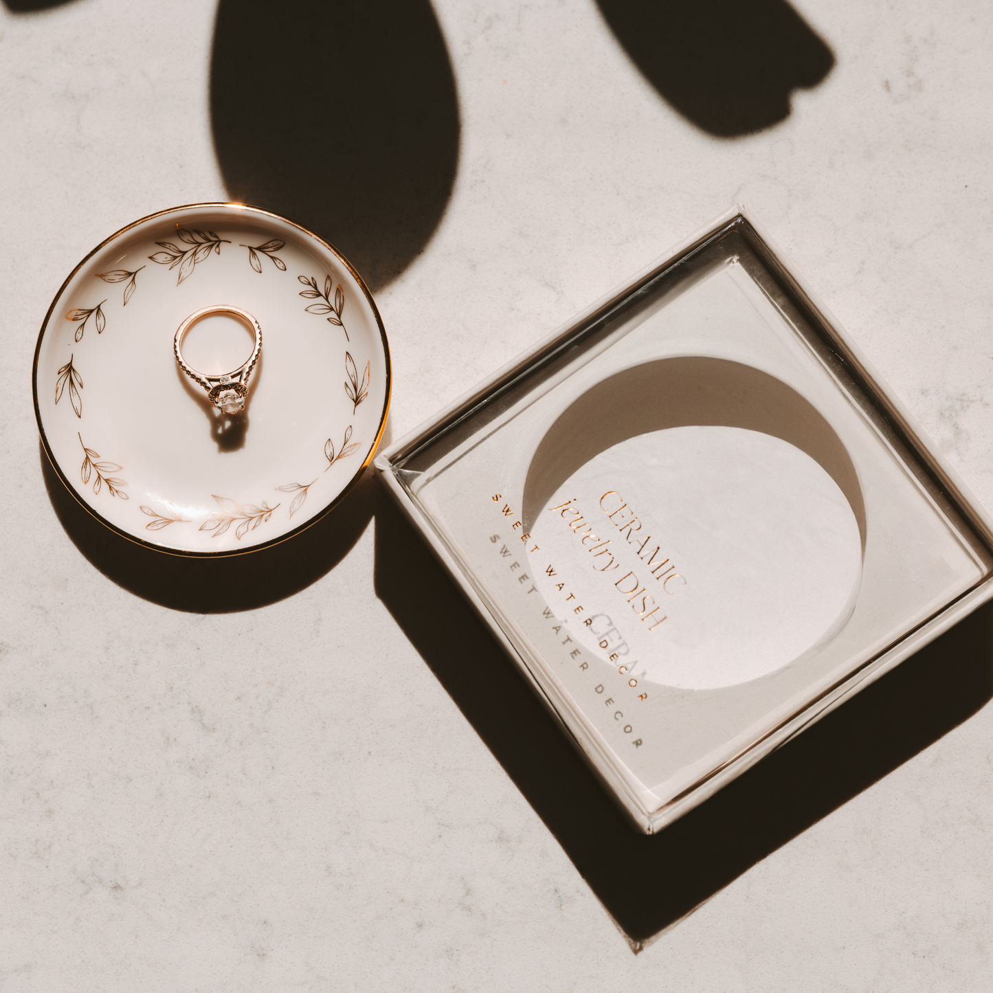 Gold ring on a decorative ceramic dish with a matching box on a light background