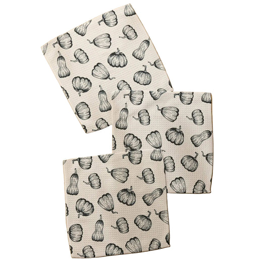 Three square kitchen towels with a black and white pumpkin pattern, arranged on a light wood background.
