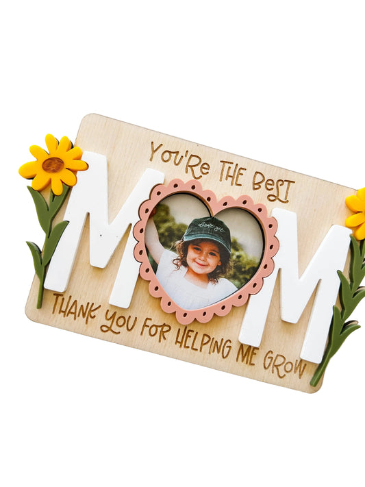 Personalized photo frame with 'MOM' and a heart-shaped inset of a child, surrounded by flowers on a light background.