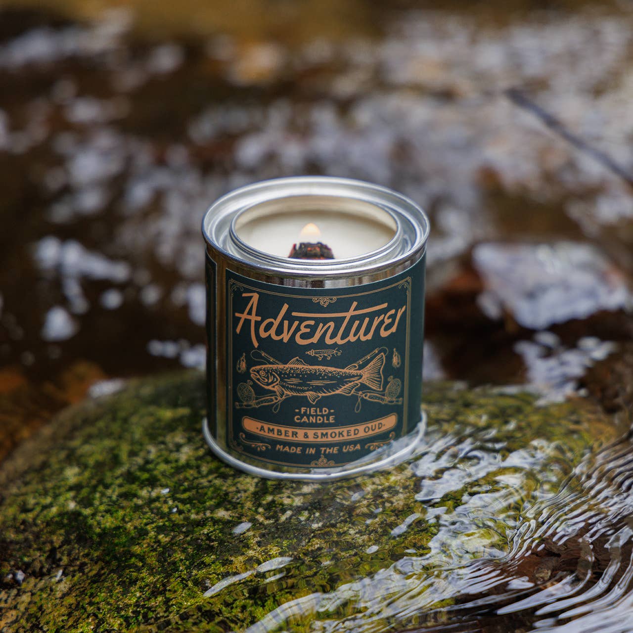 Candle in a can labeled 'Adventures' on a rock with a natural background