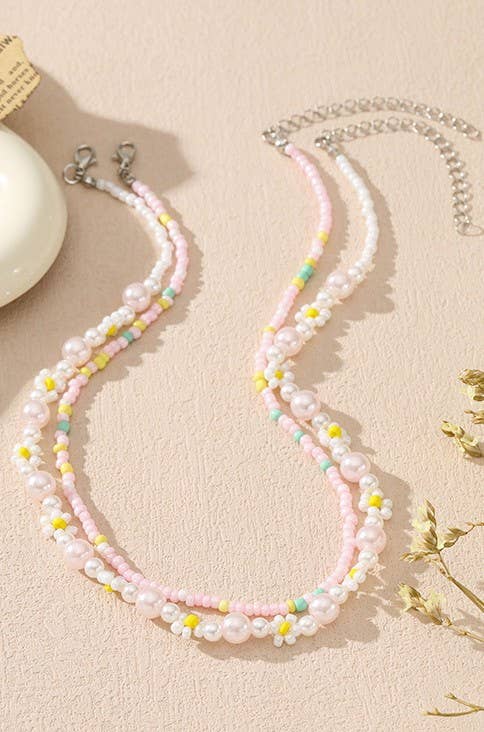 Pastel beaded necklace on a beige surface with earrings and a decorative object.