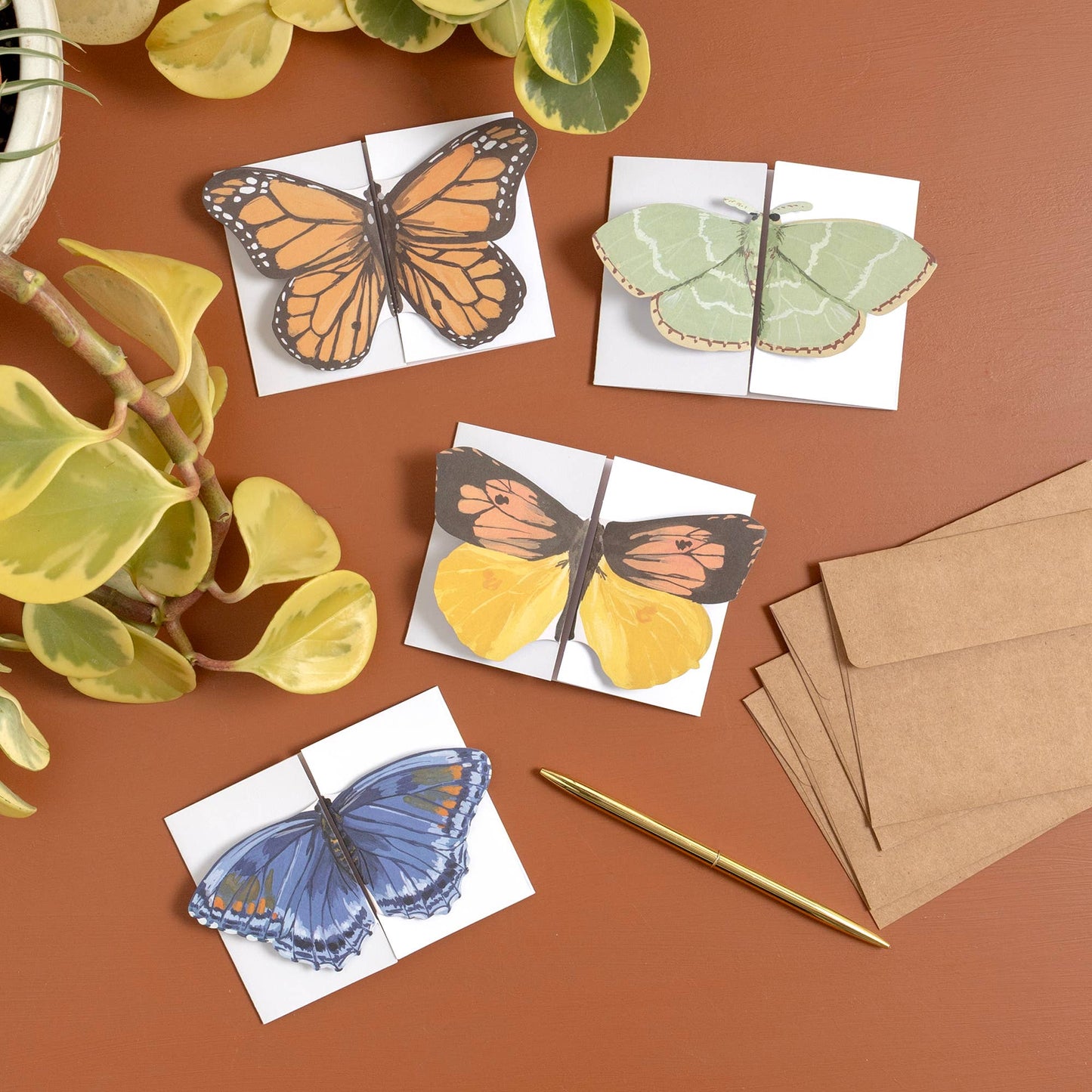 Butterfly-themed cards on a brown surface with envelopes and a pen.