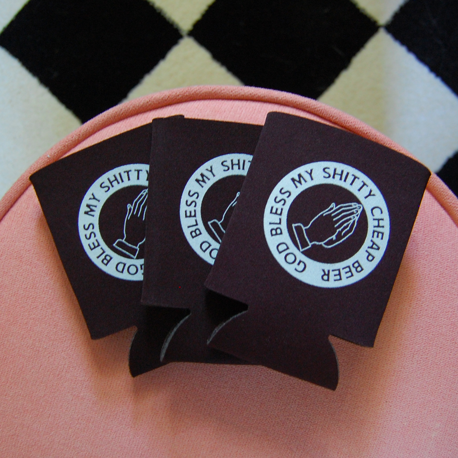 Three black can coolers with a printed design on a pink surface.