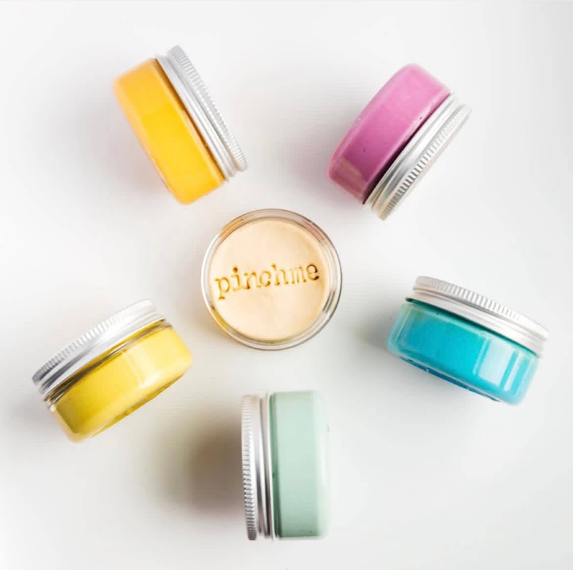 Colorful jars with silver lids on a white background, featuring the brand 'pinchme'.