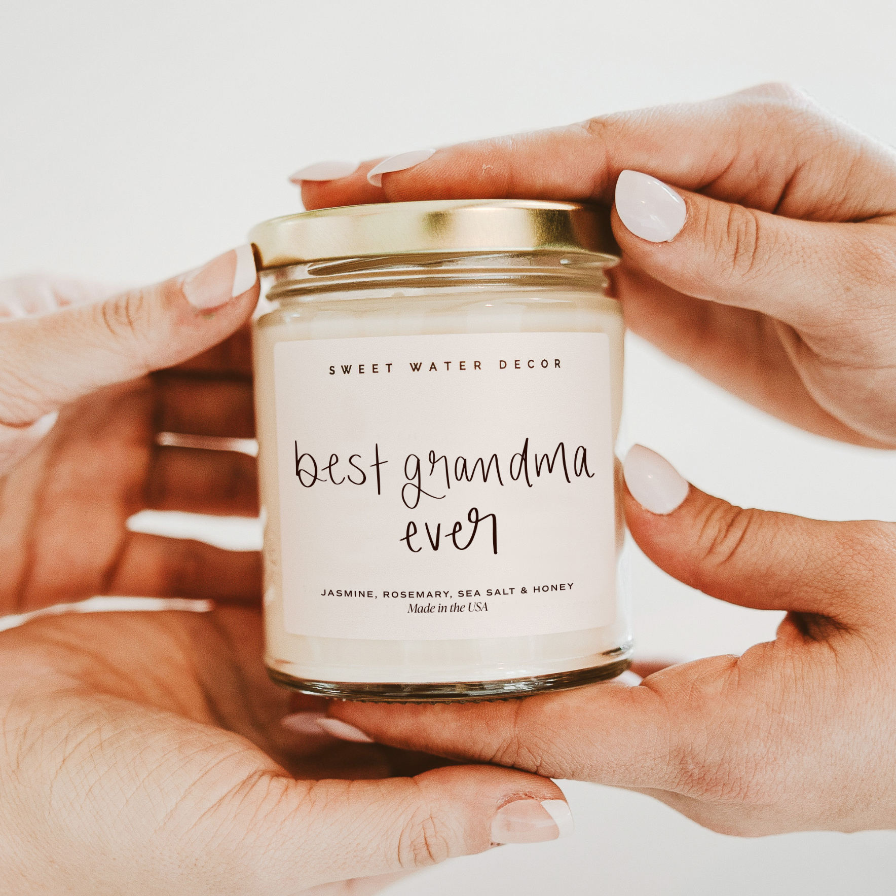 Jar of 'best grandma ever' candle held by hands with a light background