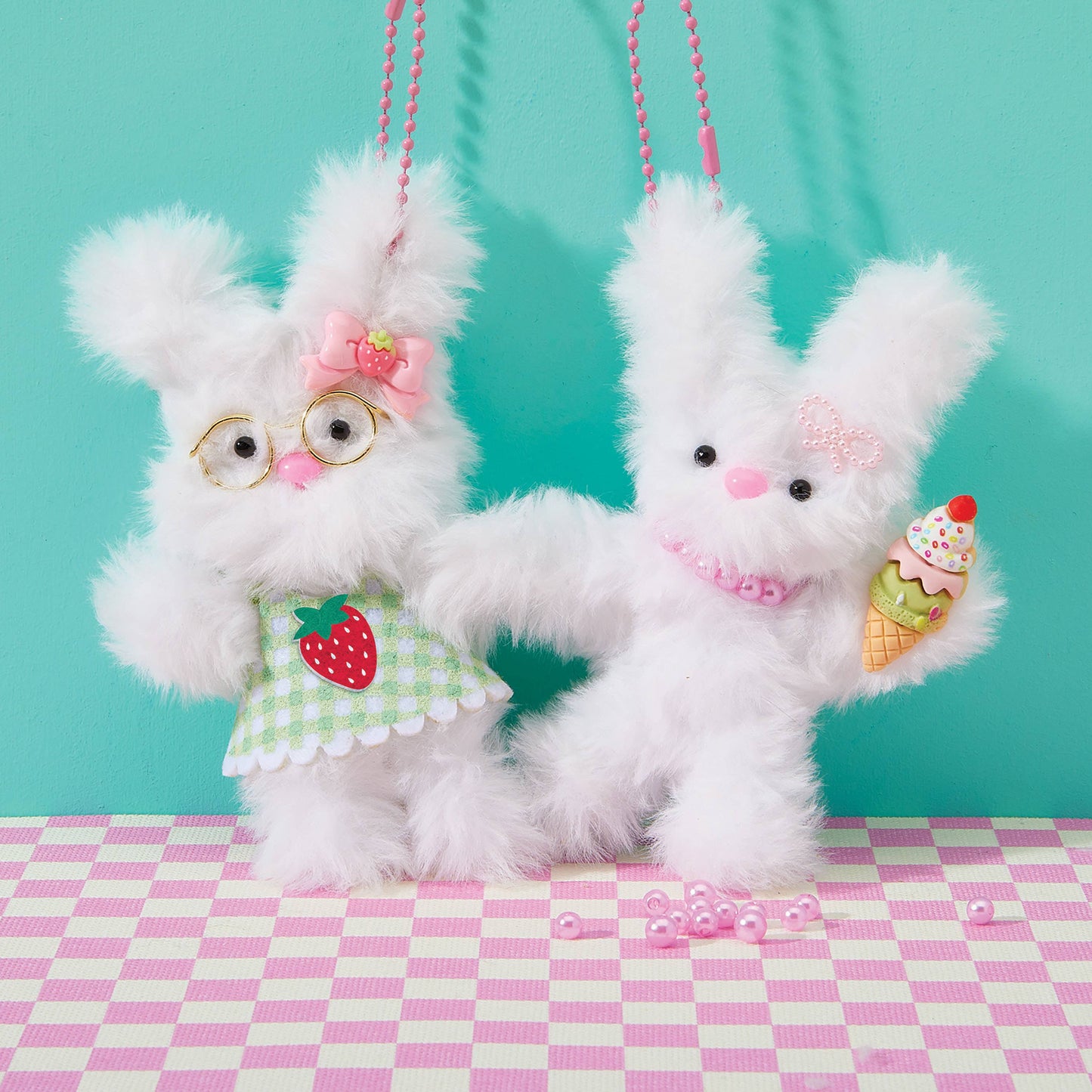 Two fluffy white rabbit toys with accessories on a checkered pink and white surface against a teal background.