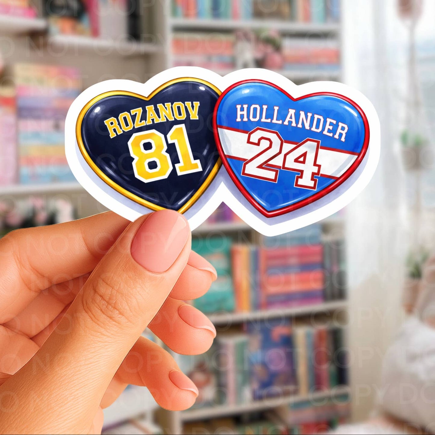 Heart-shaped stickers with text held by a hand in front of bookshelves.