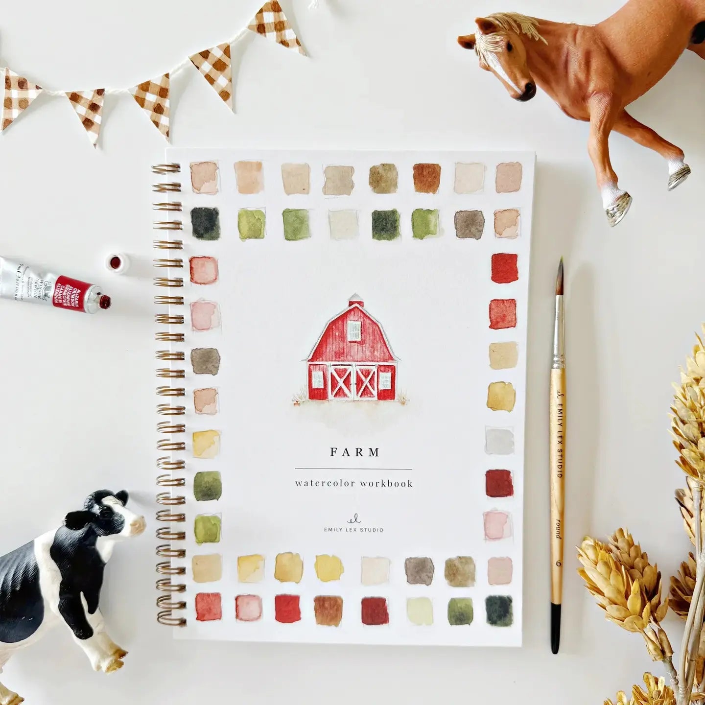 Notebook with farm-themed cover and color swatches, surrounded by decorative items on a white surface.