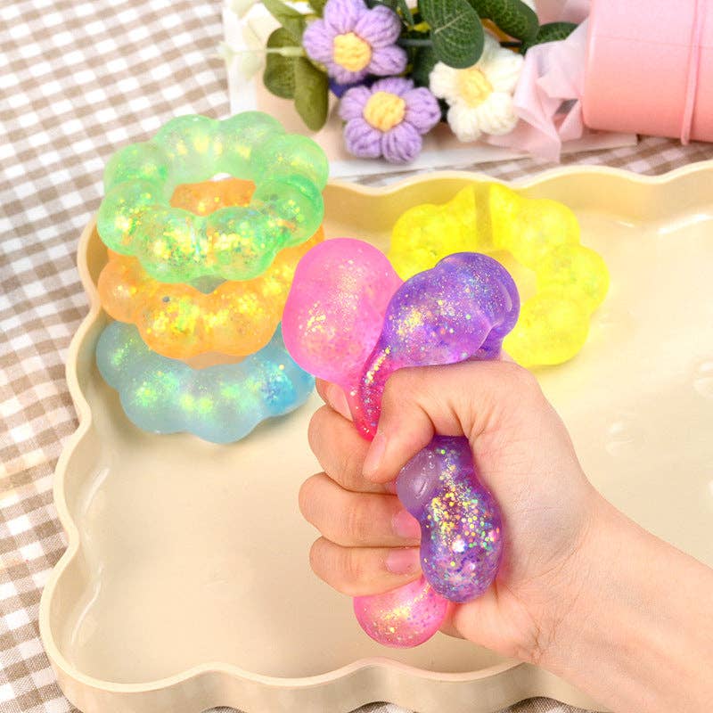 Colorful glittery stress ball held by a hand with a decorative tray and flowers in the background.