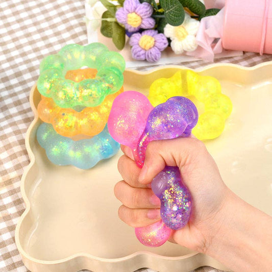 Colorful glittery stress ball held by a hand with a decorative tray and flowers in the background.