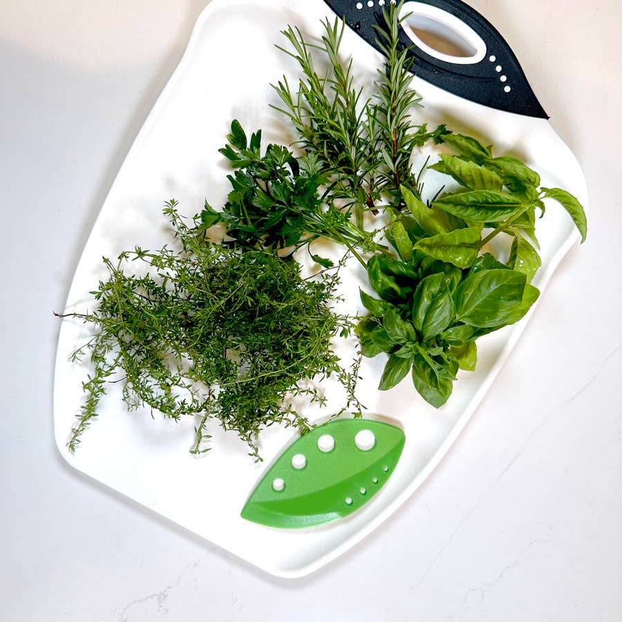 Assorted fresh herbs on a white cutting board with a green leaf design.