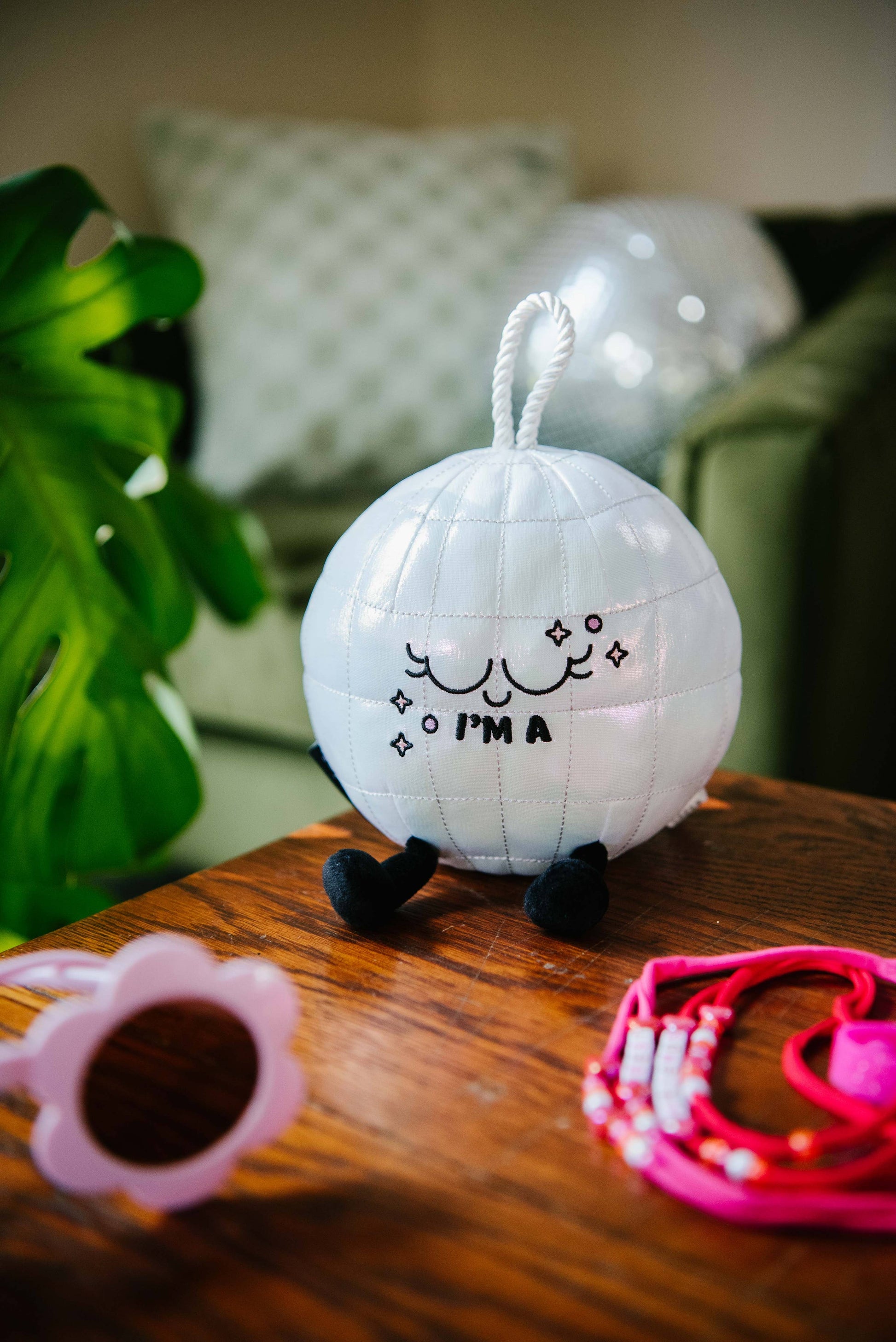 White decorative ball with a smiley face and text on a wooden surface with a plant and pillows in the background.