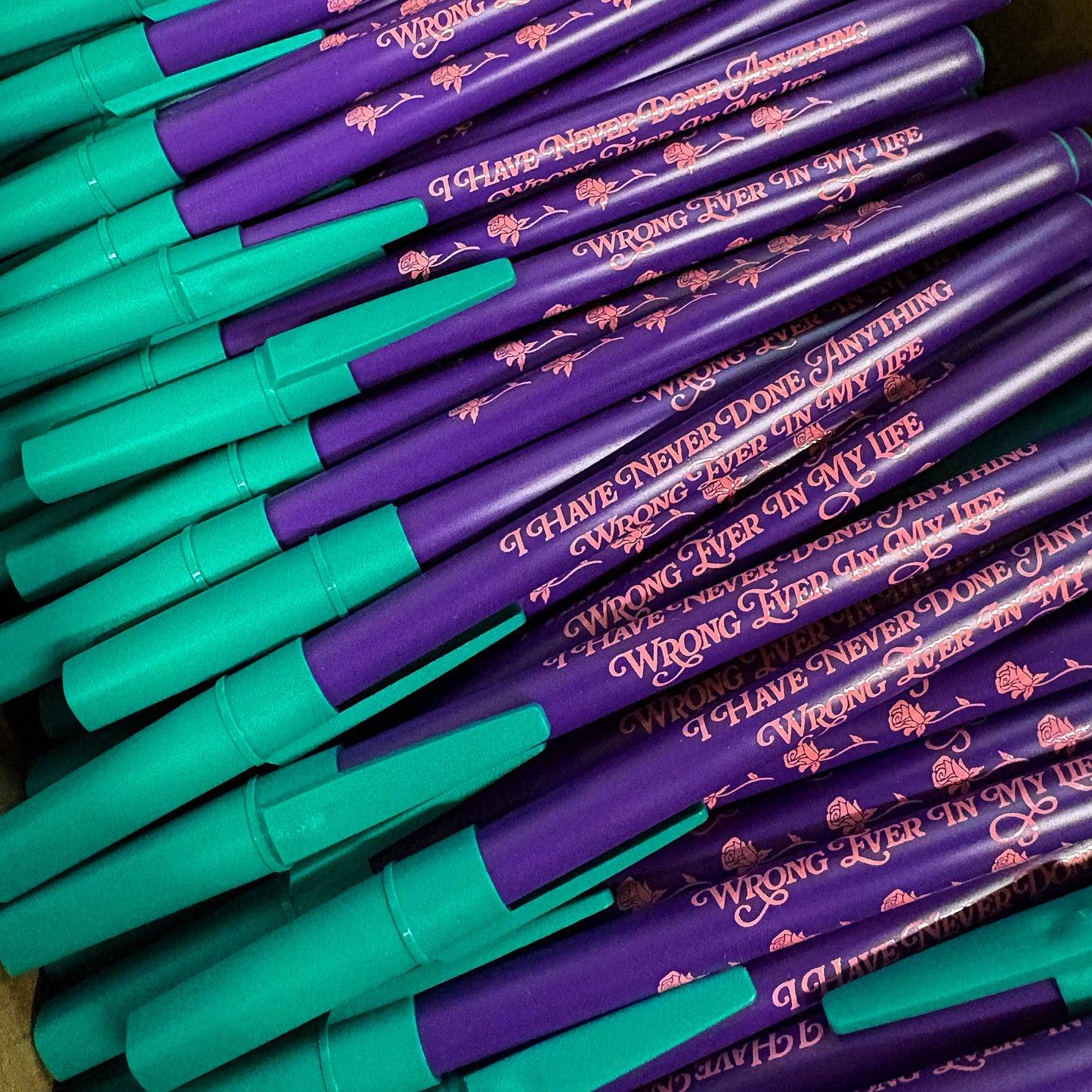 Stack of green and purple pens with humorous text on a plain background