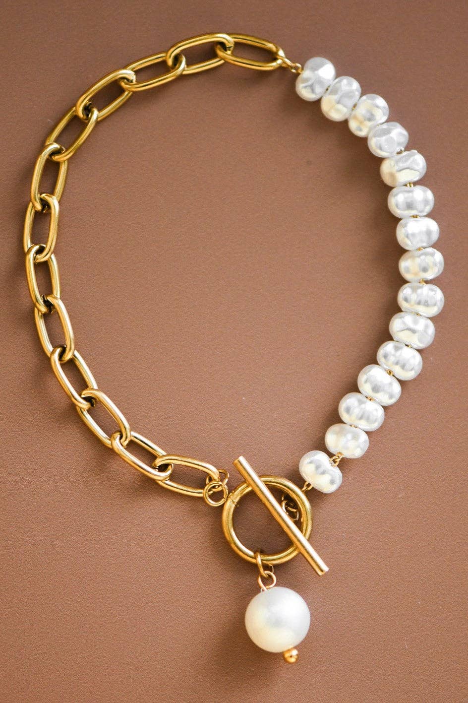 Gold chain bracelet with white pearls on a brown background