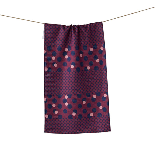 A rectangular fabric panel or curtain with a geometric polka dot pattern in dark blue, magenta, and light pink, hanging from a thin string against a plain light gray wall.